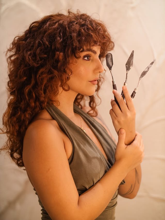 Gabi Rodrigues de perfil segurando três espátulas de pintura