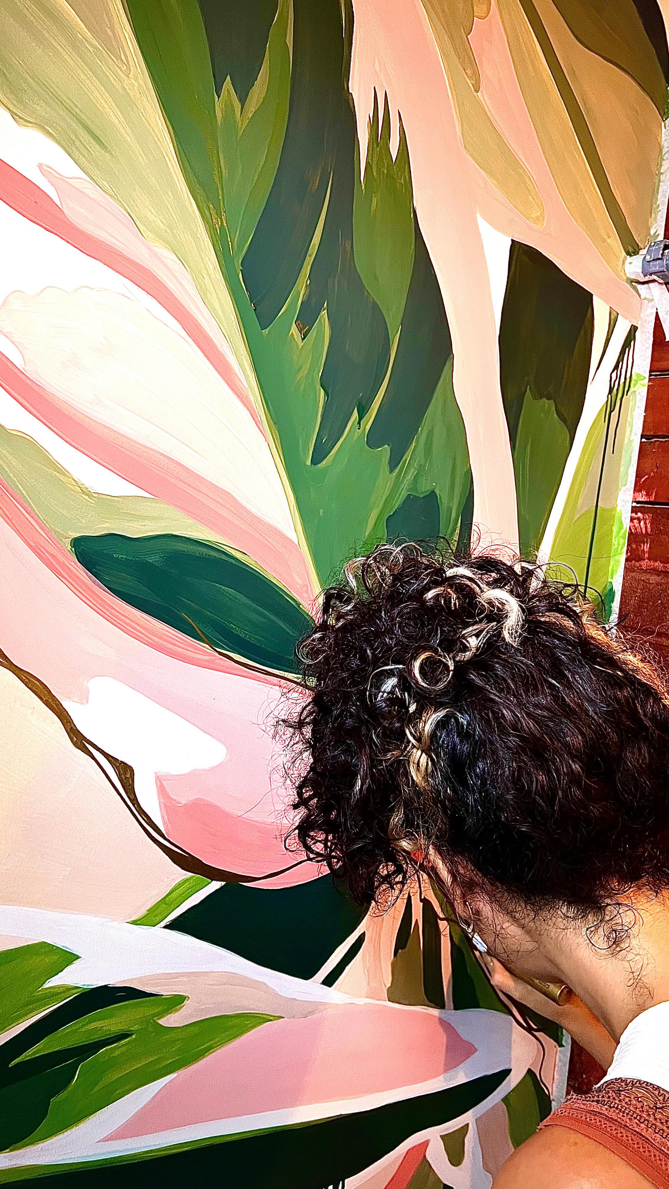 Gabi Rodrigues paints a mural with leaves in green and pink