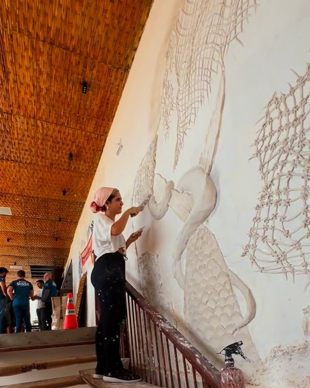 Gabi Rodrigues modelling a relief panel on the wall of a beachfront bar, under a thatched roof